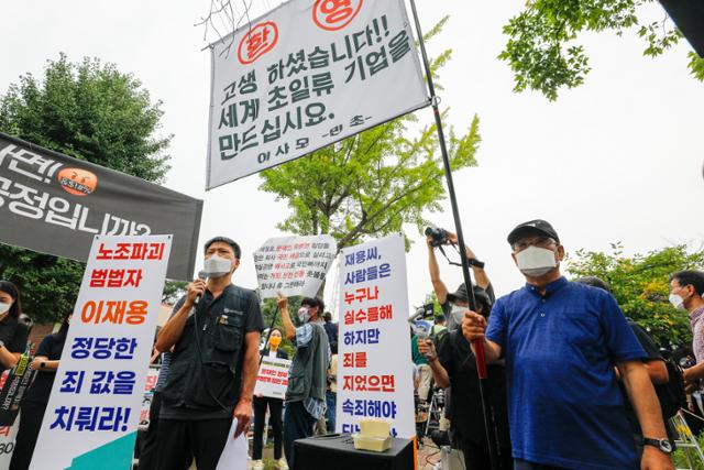 정주교 전국금속노동조합 부위원장이 13일 오전 경기 의왕 서울구치소 앞에서 열린 이재용 특혜 가석방 규탄 기자회견에서 발언하는 중 이 부회장의 가석방을 환영하는 시민이 옆에 깃발을 들고 서 있다. 뉴스1