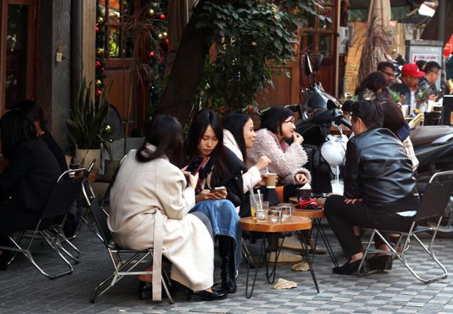 People sit on low outdoor stools, drinking coffee and chatting, in Hanoi, Vietnam. Hankook Ilbo