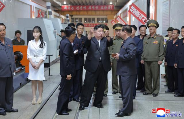 Kim Ju-ae, daughter of the North Korean leader Kim Jong-un, is seen standing to the side while the crowd next to her father listens attentively to him speak during thier visit to a key munitions factory in June 2025. Korean Central News Agency