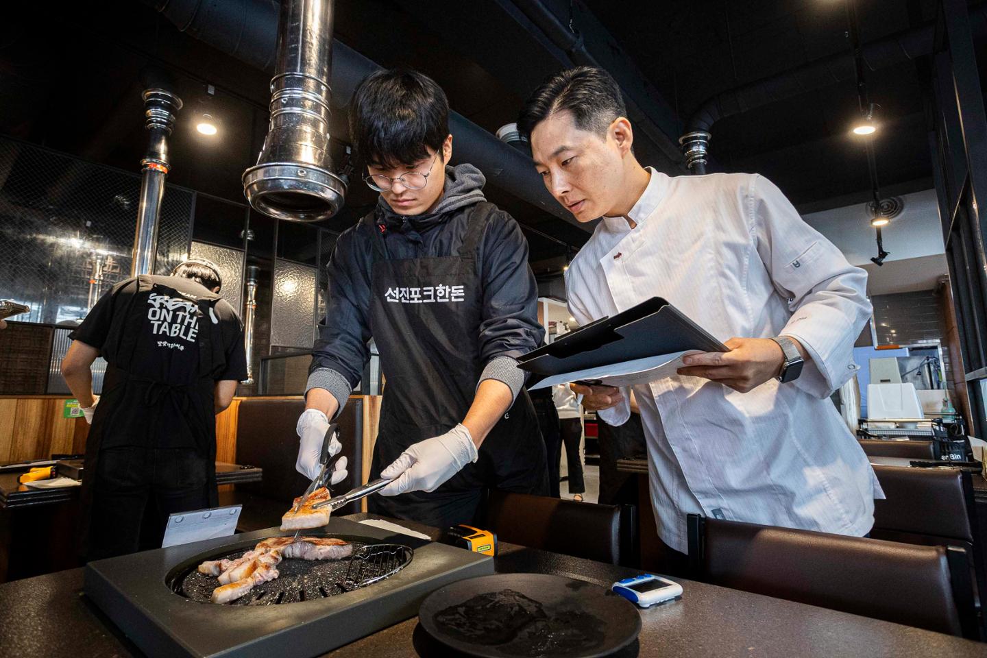 Cha Ho-myung, right, head of the Food Solution Team at Sunjin Technology Research Institute's Meat&Food Innovation Center, evaluates a participant's grilling technique during the 19th Grilling Meister certification exam at Yaksan Dwaeji in Yeongdeungpo District, Seoul, Oct. 14. Courtesy of Sunjin